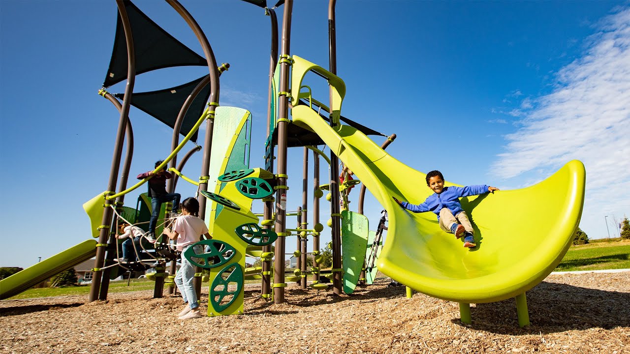 Child sliding on a bright green playground slide under blue sky. Fun outdoor play area for kids.