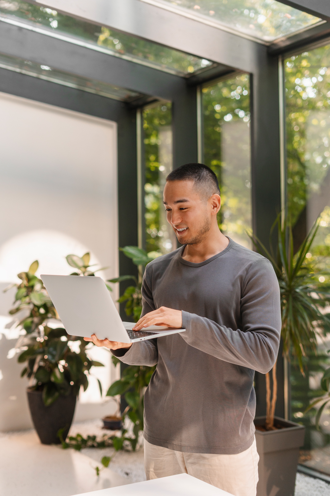 Person smiling and using a laptop in a bright room with plants, enjoying a productive work environment.