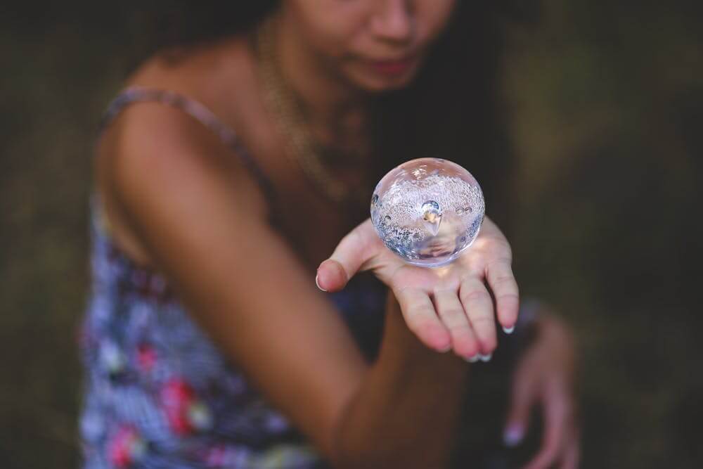 Woman holding a crystal ball in an open palm, showcasing reflection and clarity.